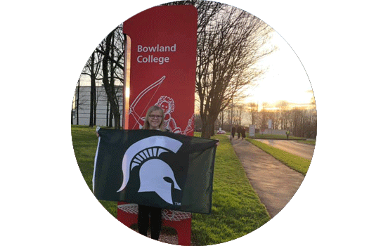 Student holding Spartan flag in front of sign that reads Bowland College