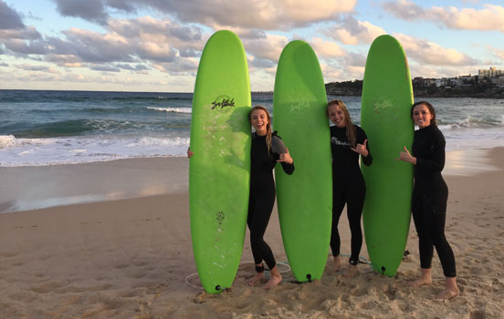 Students on beach holding surfboards in Sydney, Australia