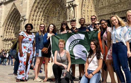 Group of students holding Spartan flag in front of cathedral in Italy