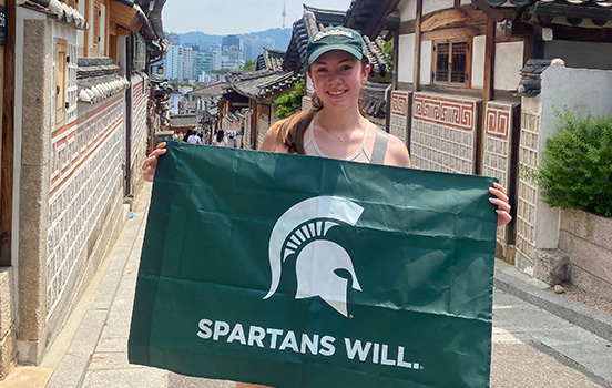 MSU student holding Spartan flag on a street in Seoul, South Korea