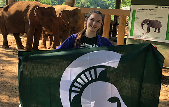 Student holding Spartan flag at elephant sanctuary in Thailand